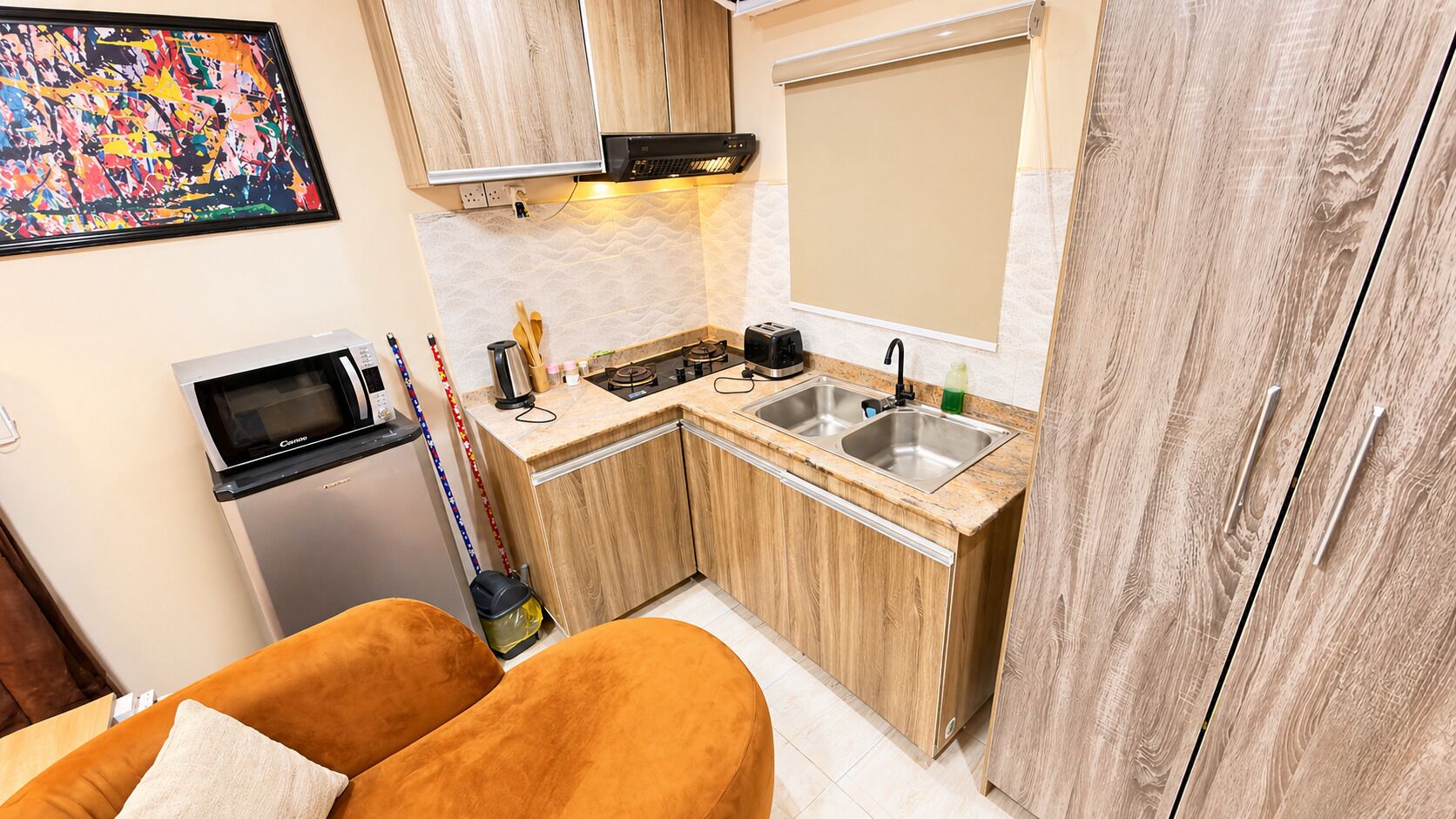 A compact kitchen with wooden cabinets, a microwave, a sink, and a countertop with various kitchen items.