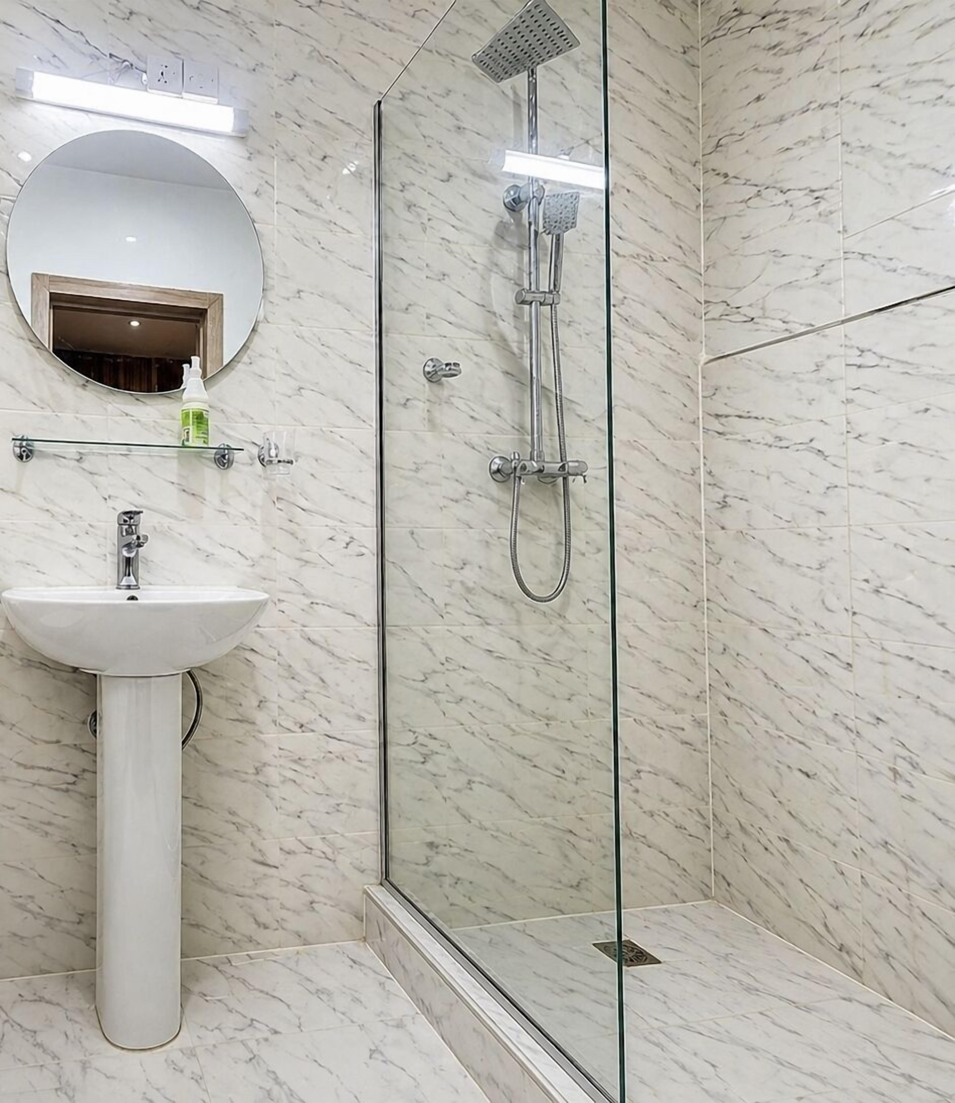 A bathroom with a glass-enclosed shower, a pedestal sink, and a round mirror.