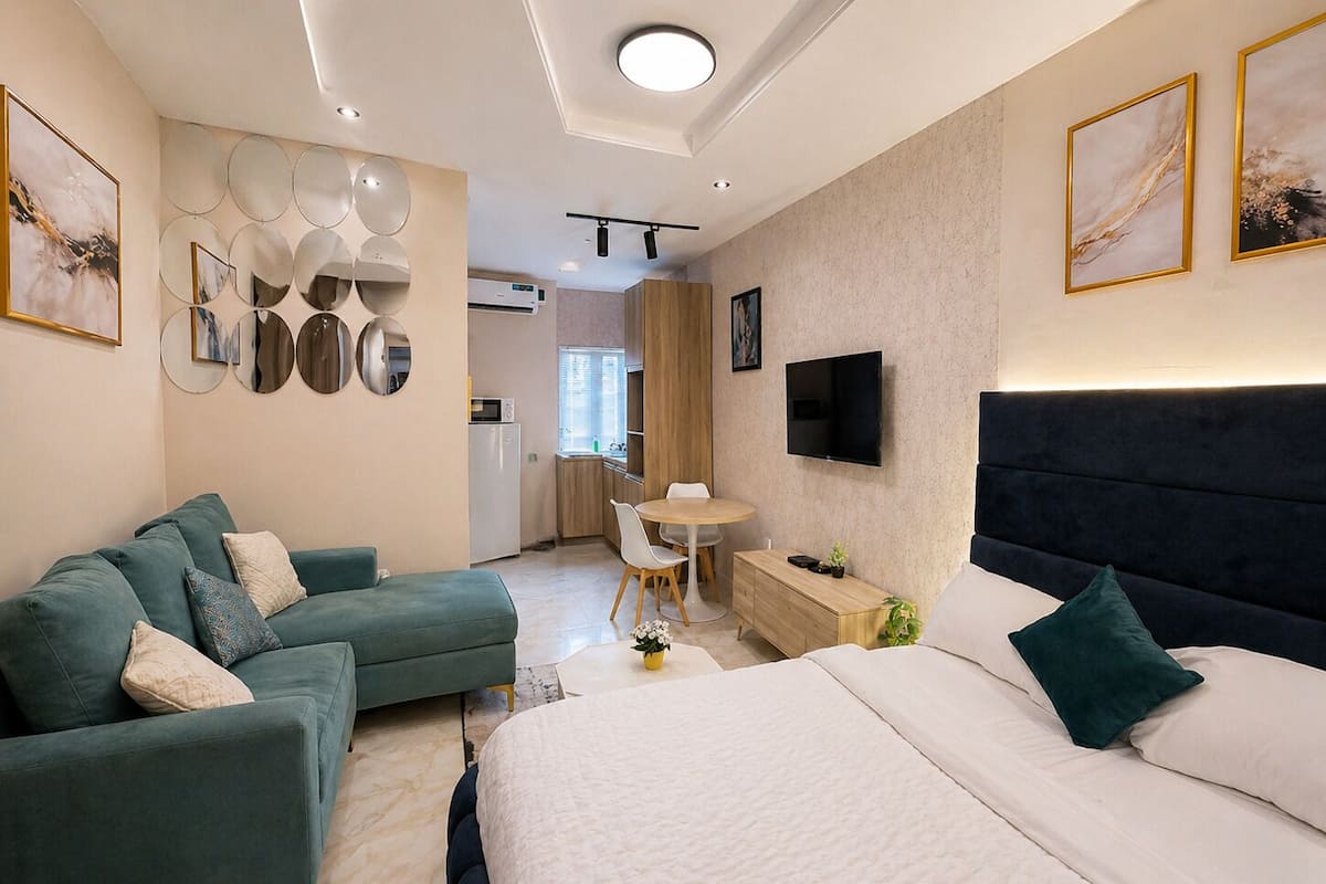 Quarto de hotel moderno com cama, sofá, televisão e área de refeições.