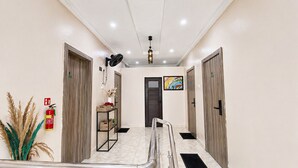 A hallway with a fire extinguisher, a wall-mounted fan, a door with a colorful artwork, and a metal handrail. - Happy Lodge Shortlets & Suites (Lekki)