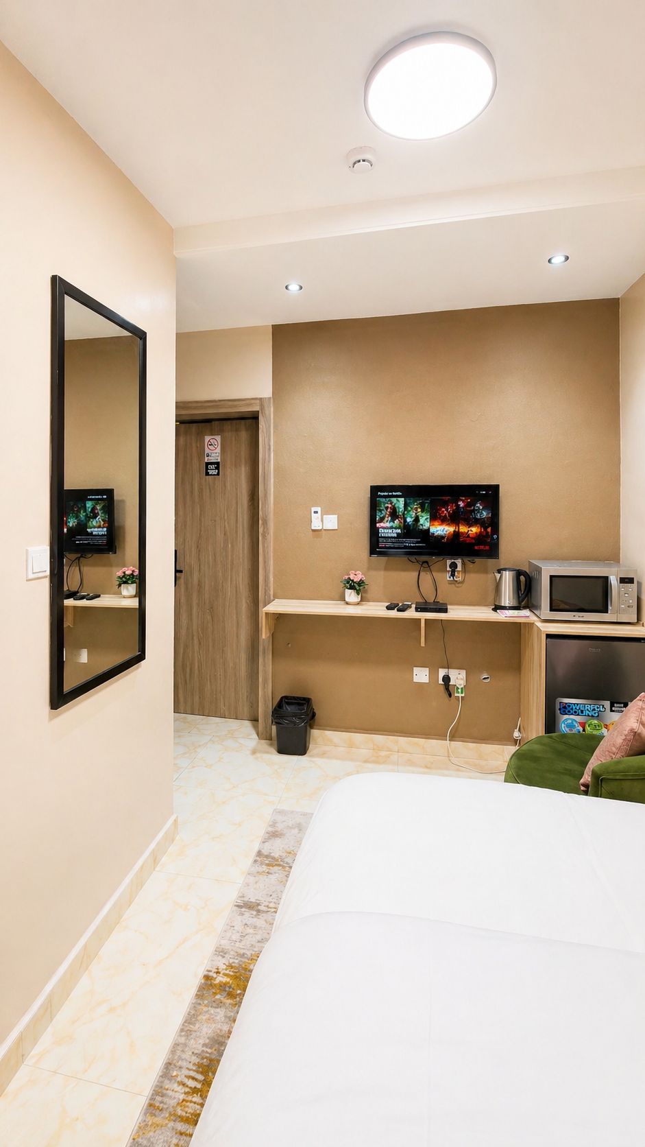 Une chambre d’hôtel avec un lit, un téléviseur fixé au mur, un four à micro-ondes, une petite poubelle et une porte avec une pancarte.