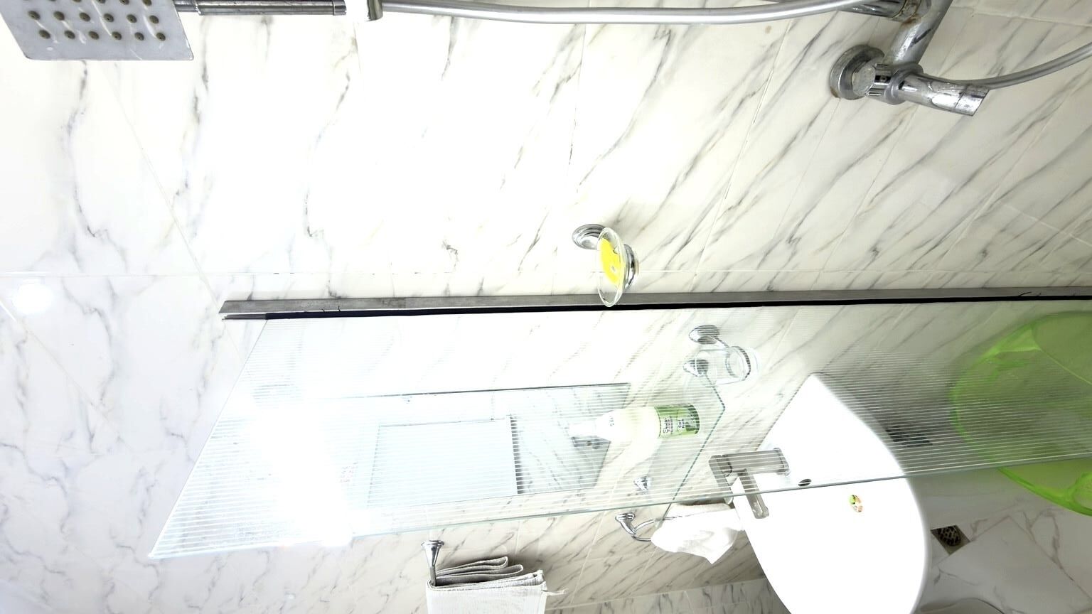 A bathroom with a marble floor, a glass shower enclosure, and a visible toilet.