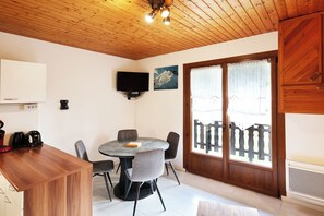 A dining area with a round table, chairs, a television mounted on the wall, and a wooden ceiling. - Quiet apartment, ideal for a relaxing stay. (Gérardmer)