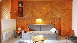 Une pièce avec un plafond en bois, un canapé gris agrémenté de coussins, une petite table en bois et des placards encastrés en bois.