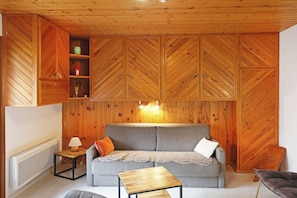 A room with a wooden ceiling, a grey sofa with cushions, a small wooden table, and built-in wooden cabinets. - Quiet apartment, ideal for a relaxing stay. (Gérardmer)