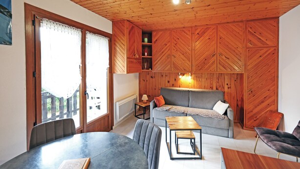 Une pièce avec un plafond en bois, un canapé gris, une table à manger et une chaise.