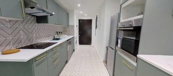 Een smalle keuken met een backsplash van visgraat tegels, een aanrecht met een snijplank en een koelkast.