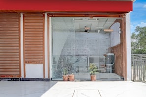 A building entrance with a sliding glass door, potted plants, and a visible interior space with a ceiling fan.