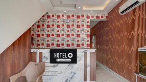 A hotel reception desk with a 'HOTELO' sign, a patterned wall, and a wooden slat wall.