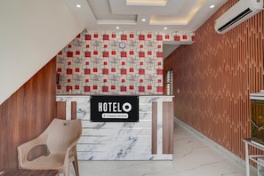Un comptoir d’accueil d’hôtel avec une enseigne « HOTELO », un mur orné de motifs et un mur composé de lattes de bois.