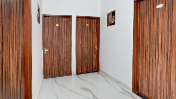 A hallway with two wooden doors, a small framed picture on the wall, and a marble floor.
