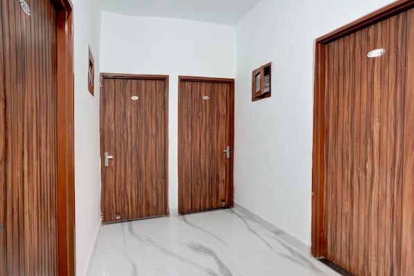Un pasillo con dos puertas de madera, un pequeño cuadro en la pared y un suelo de mármol.