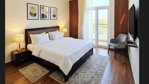 A hotel bedroom with a bed, bedside lamps, a ceiling fan, a TV, a chair, and a large window. - 4-bedroom house in delightful Coimbatore with cool AC and space (Coimbatore)