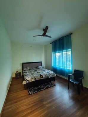 A bedroom with a bed, a ceiling fan, a chair, and a window with curtains.