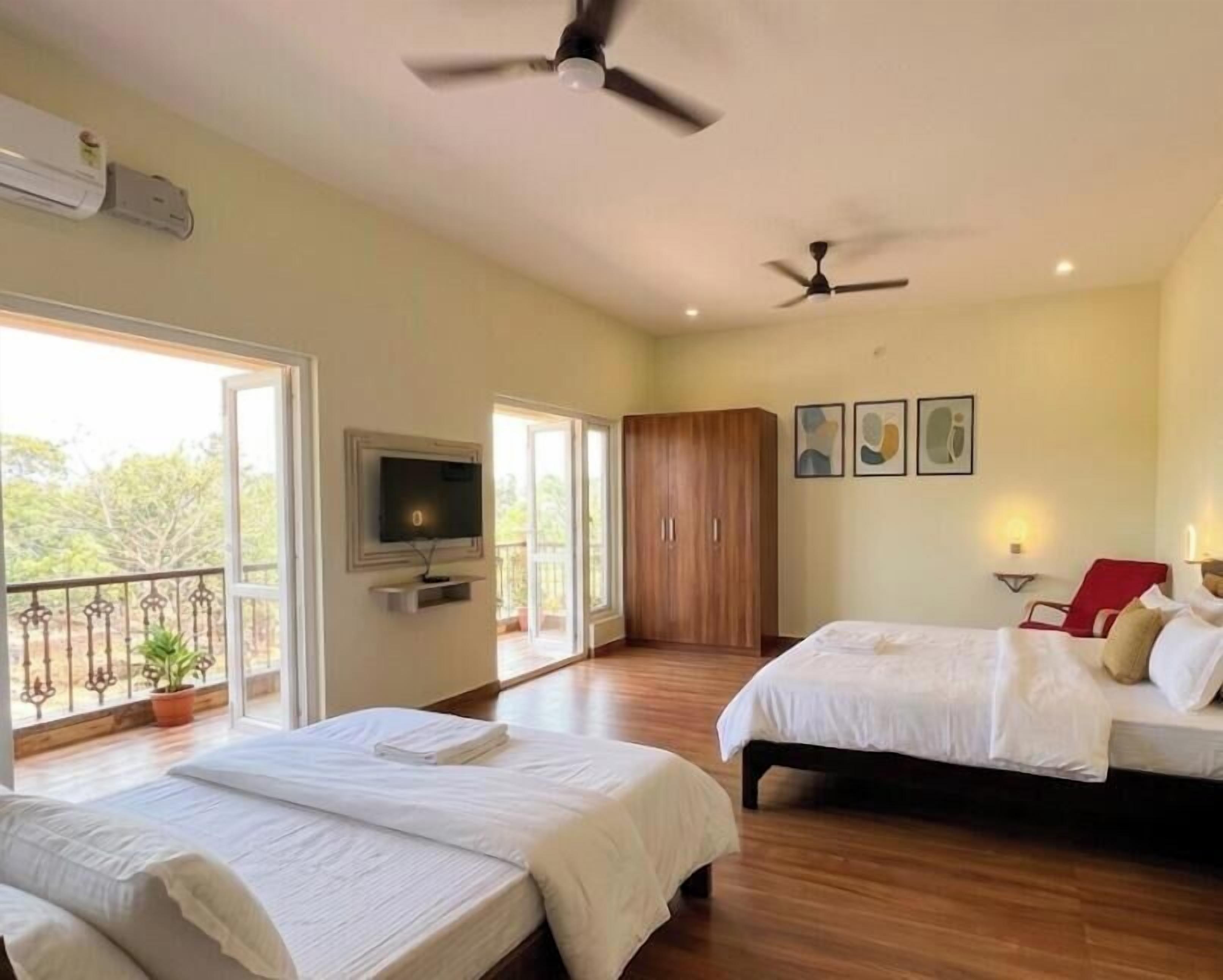Une chambre d’hôtel avec deux lits, une télévision, un balcon et un ventilateur de plafond.