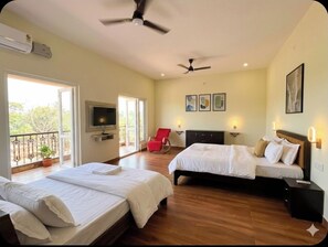 Habitación de hotel con dos camas, televisor, balcón con planta en maceta y una obra de arte en la pared.