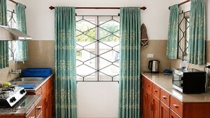 Una cocina con mesa, armarios, estufa y una ventana con cortinas.