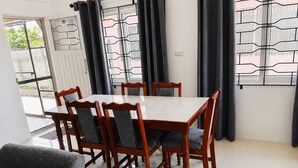 Un comedor con una mesa rectangular y seis sillas, una ventana con barrotes, y una puerta que da al exterior.