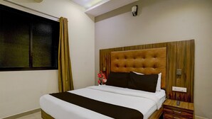 A hotel room with a large bed, a nightstand, a wall-mounted light, and a window with curtains.