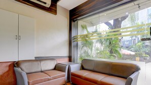 A modern waiting area with two leather sofas, a white cabinet, and a large window with a view of greenery and buildings.