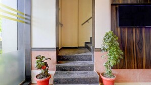 A staircase leading to a room with a wooden door, two potted plants, and a flat-screen TV mounted on the wall.