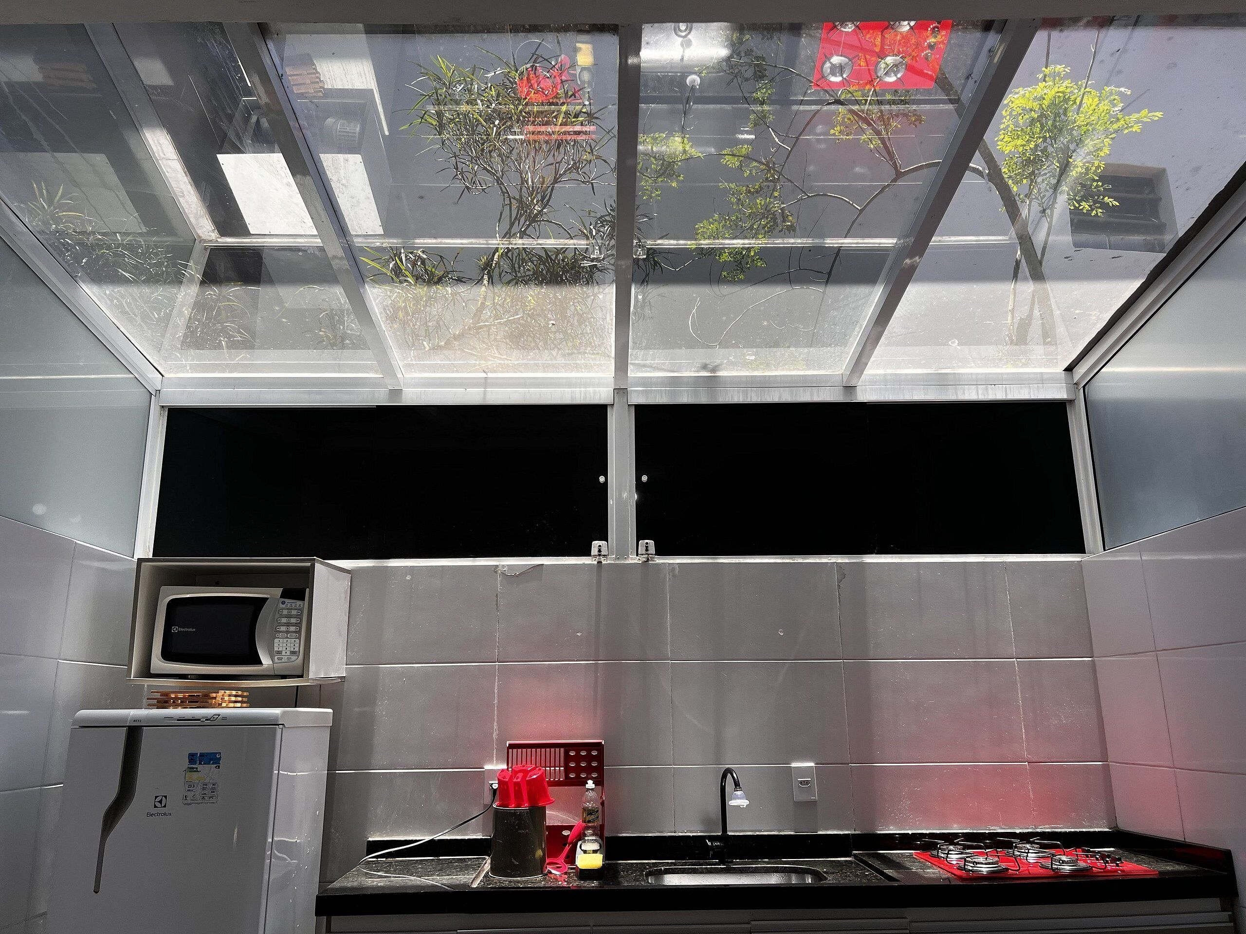 Een keuken met een magnetron, spoelbak en kookplaat, een dakraam en uitzicht op bomen.
