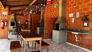 Un espacio exterior para comer con paredes de ladrillo, mesas y bancos de madera, un horno de leña y adornos colgantes.