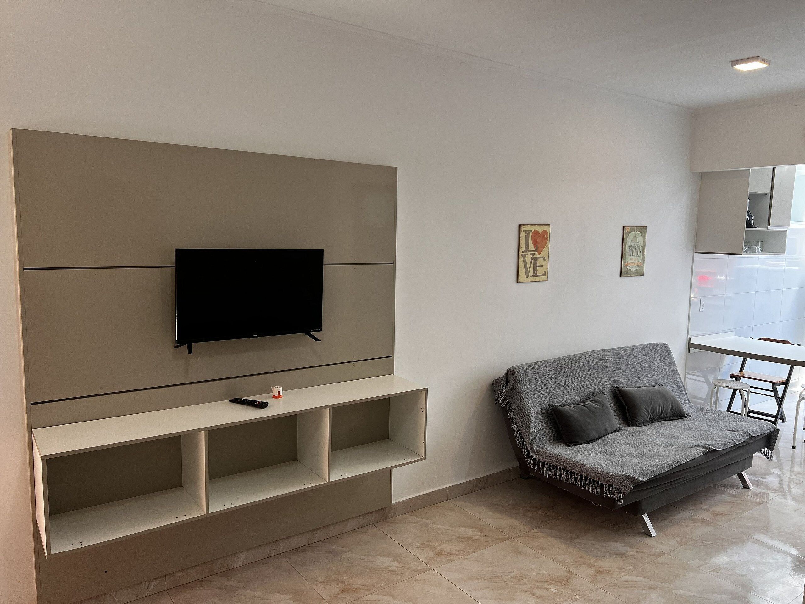 A modern living room with a flat-screen TV mounted on a wall, a grey sofa, and a small table.