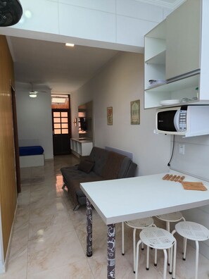 A compact living space with a kitchenette, a sofa, a dining table, and a small TV.