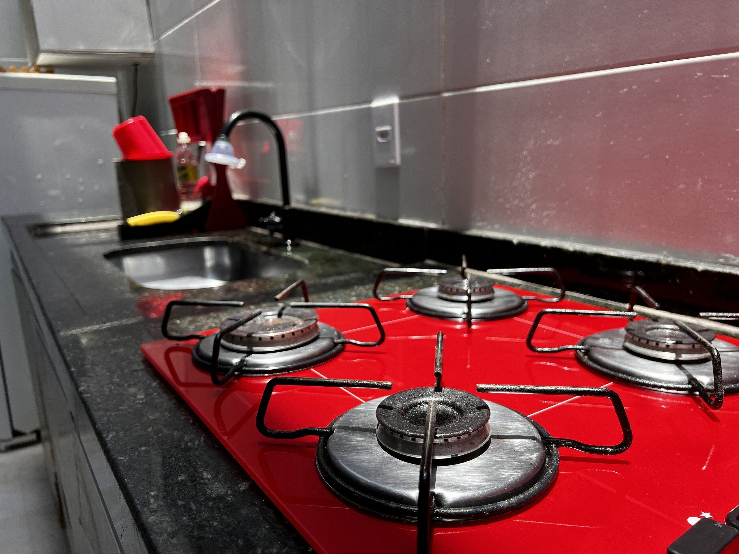 Una cocina con estufa a gas roja, un lavaplatos de acero inoxidable y un portalápices rojo.