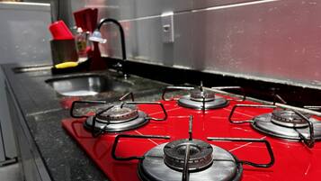 Una cocina con estufa a gas roja, un lavaplatos de acero inoxidable y un portalápices rojo.