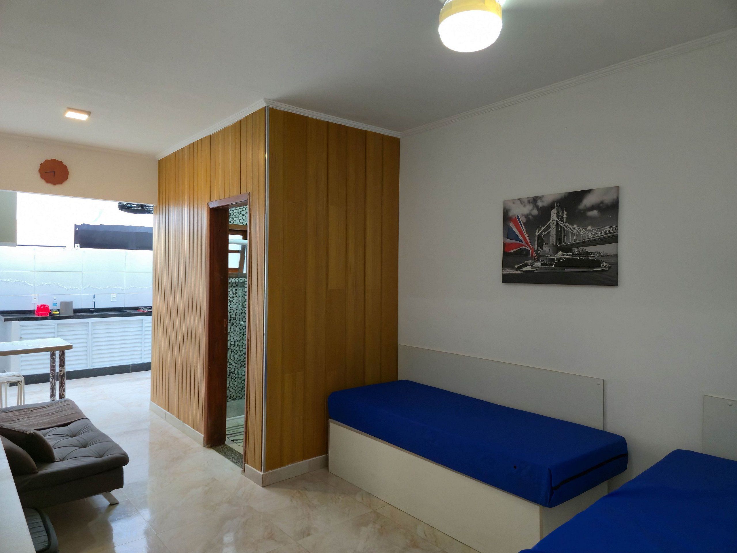 Una habitación con separador de madera, una cama con ropa de cama azul, un banco y un cuadro colgado en la pared.