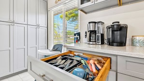 Una cucina con mobili bianchi, una macchina da caffè, un bollitore e un organizer per cassetti.