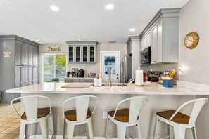 Une cuisine moderne avec des meubles gris, un grand îlot central doté de tabourets, une machine à café et une horloge au mur.