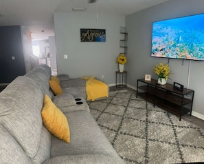 A living room with a gray sofa, yellow pillows, a TV, and a wall with a 'HELLO gorgeous' sign. - Cozy family home minutes from Disney, fully equipped with Wi-Fi, pool… (Kissimmee)