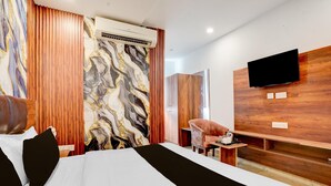 A hotel room with a large bed, a TV mounted on the wall, a wooden vanity, and a marble-patterned wall. - Collection O Zirakpur Bus Terminal (Dera Bassi)