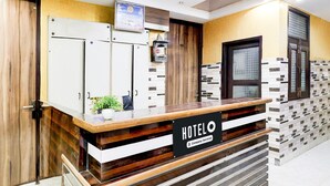En hotellreception med en skylt med texten ”HOTELO”, en växt och en vägg täckt med kakel.