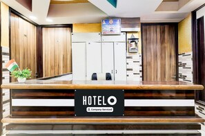 A hotel reception desk with a sign indicating it is company-serviced. There are wooden doors and a framed picture on the wall. - Deluxehotel Welcome Inn (New Delhi)