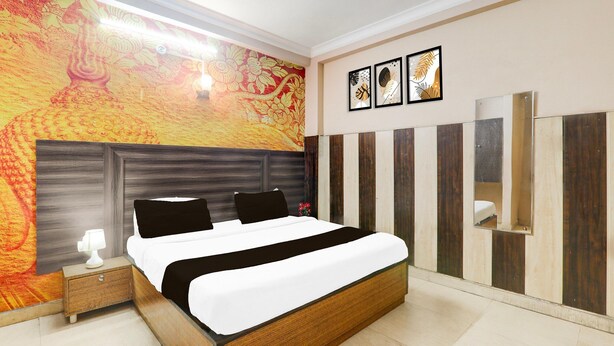 A modern bedroom with a large bed, a nightstand, a wall tapestry, and a wooden panel wall. - Saver Double Sharda Nagar Lucknow (Lucknow)