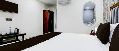 Una habitación de hotel con una cama, un escritorio, un espejo, un equipo de aire acondicionado y una ventana.