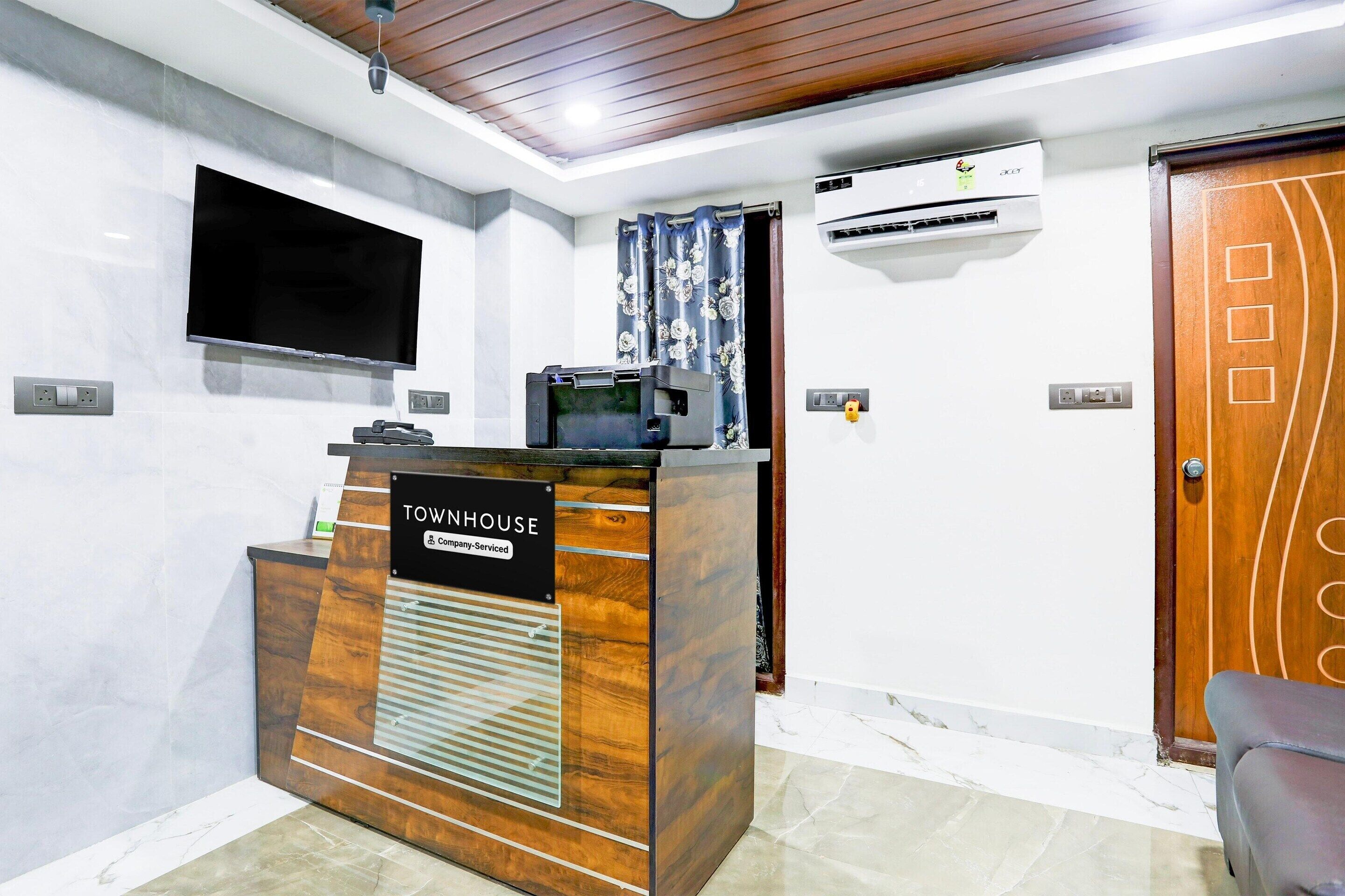 A reception desk with a sign reading 'TOWNHOUSE,' an air conditioning unit, a mounted television, and a door with a decorative panel.