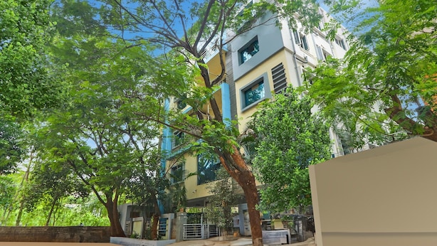 A multi-story building with a modern architectural design, surrounded by lush green trees. - Deluxe Townhouse VIP Hills Hitech City (Hyderabad)