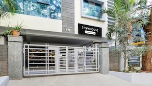 A townhouse with a gated entrance, a sign indicating it is company-serviced, and a view of the surrounding area including a tree and a building in the background. - Deluxe Townhouse VIP Hills Hitech City (Hyderabad)