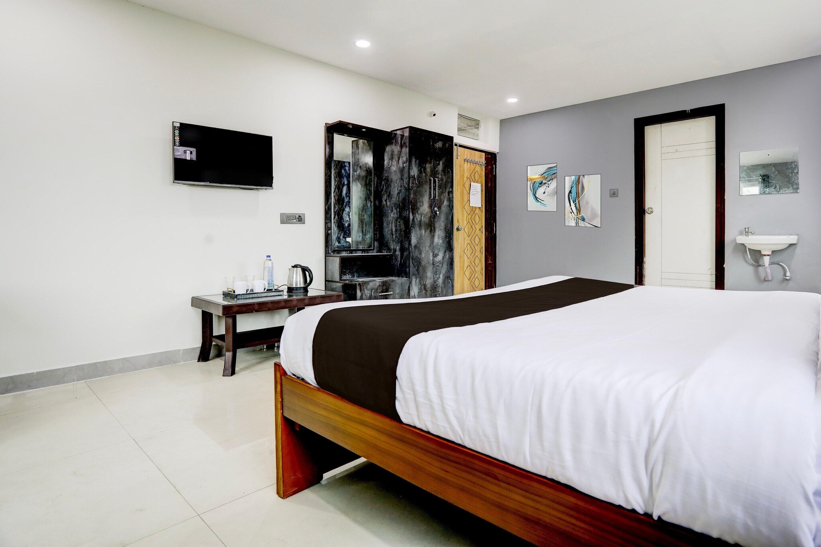 Quarto de hotel com cama, televisão, escrivaninha com cadeira, espelho e pia.