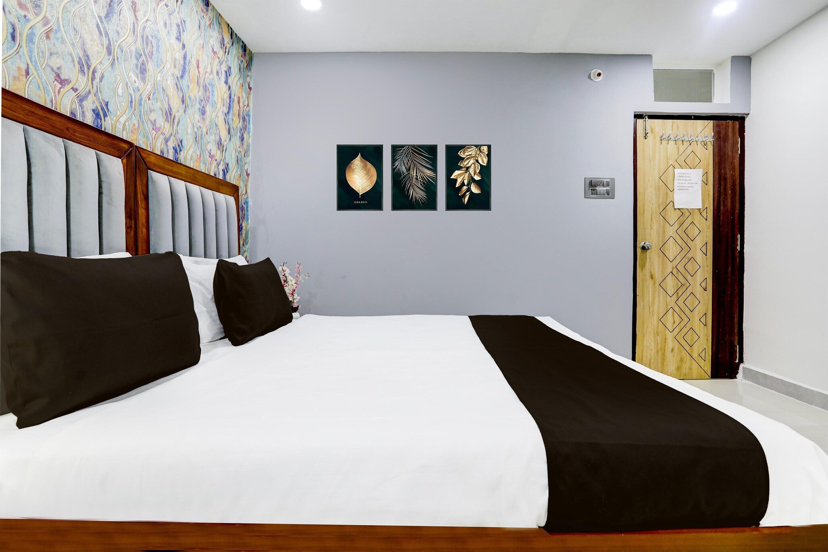 Un dormitorio con cama, cabecero de madera, pared con tres láminas enmarcadas de hojas, y una puerta con diseño geométrico.