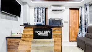 A reception desk with a sign reading 'TOWNHOUSE Company-Serviced,' a flat-screen TV mounted on the wall, an air conditioning unit, and a wooden door with a decorative design. - Deluxe Townhouse VIP Hills Hitech City (Hyderabad)