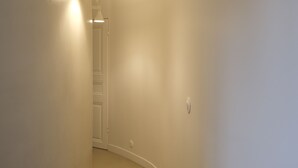 Un pasillo estrecho con una puerta al final, un aplique en la pared y un interruptor de luz también en la pared.