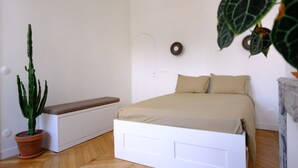 Un dormitorio con cama, una banca, planta en maceta y decoración de pared.