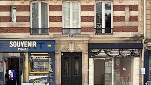 Un edificio con una tienda llamada 'SOUVENIR PIGALLE' en la planta baja, una puerta doble negra y un balcón con plantas.