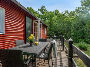 En träaltan med ett bord och stolar, en glasdörr och utsikt över ett skogsområde.
